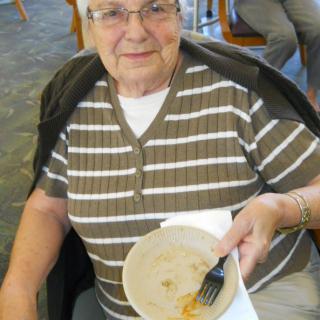 An elderly woman sitting and holding an empty plate after a meal.