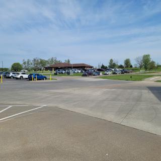 A sunny day at a park with a busy parking lot and a pavilion in the background.