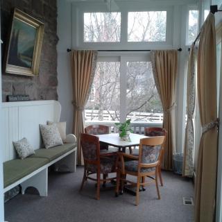 A cozy dining space with a round table surrounded by chairs, a bench for additional seating, and large windows adorned with curtains.