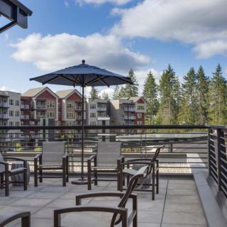A scenic patio area with chairs and an umbrella overlooking nearby buildings and trees under a partly cloudy sky.