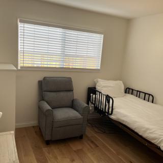 A minimalist bedroom with a single bed, recliner chair, and window with blinds.