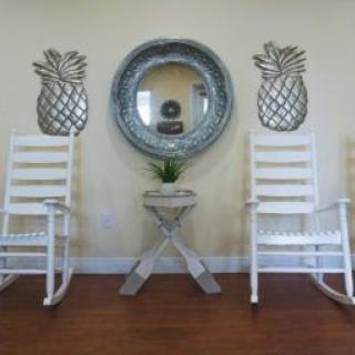 A cozy interior setup with white rocking chairs and pineapple-themed wall decor.