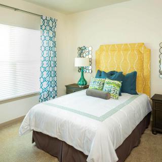 A cozy, colorful bedroom with a neatly made bed, patterned curtains, and decorative pillows.