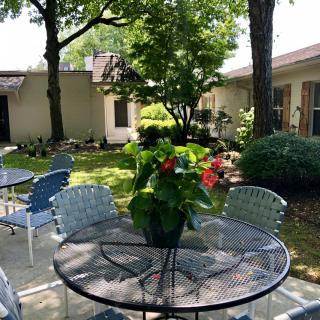 A serene garden patio with a table and chairs, surrounded by lush greenery and vibrant flowers.
