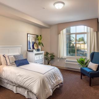 A well-lit bedroom with a single bed, armchair, and large window.