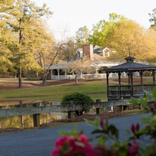 A peaceful park scene featuring a gazebo by a pond with a house in the background and colorful foliage.