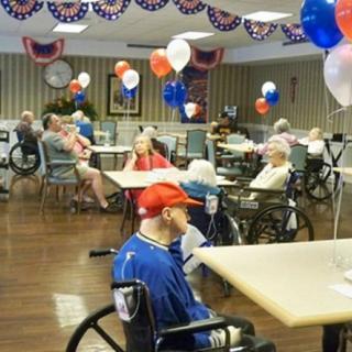 Elderly residents in a nursing home decorated with red, white, and blue balloons.