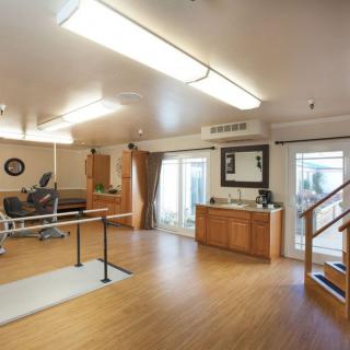 A well-lit rehabilitation room equipped with exercise equipment, including parallel bars and stairs, suitable for physical therapy.
