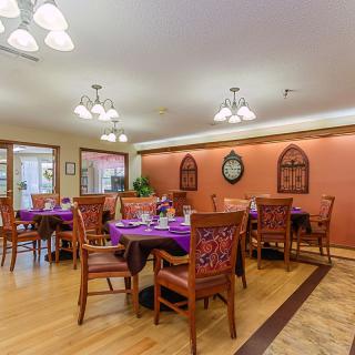 A warmly lit dining room with neatly arranged tables covered in purple tablecloths.