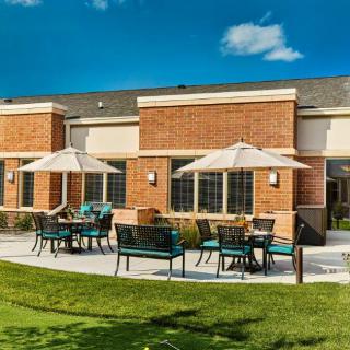 A sunny patio with outdoor seating and umbrellas in front of a brick building.