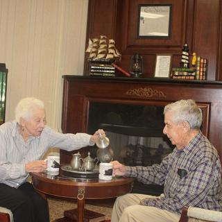 Two elderly individuals enjoying a cozy tea time conversation by the fireplace.