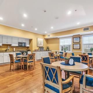 A cozy dining area with wooden floors, tables, and chairs, adjacent to a modern kitchen.