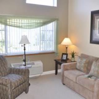 A cozy living room with a sofa, armchair, and two lamps by the window.