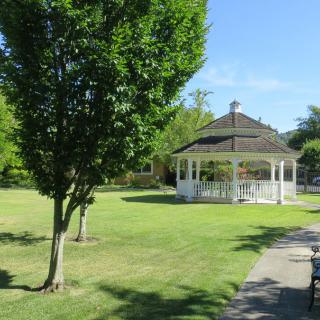 A scenic park with a gazebo, lush green grass, and trees under a clear blue sky.