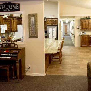 A cozy interior space featuring a hallway, kitchen area, wooden furniture, and a piano with a welcome sign.