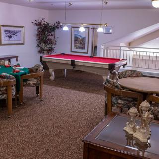 A cozy game room featuring a billiards table and card tables, complete with elegant lighting and decor.
