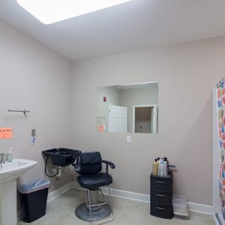 Interior of a small barbershop or salon with a chair, sink, and mirror.