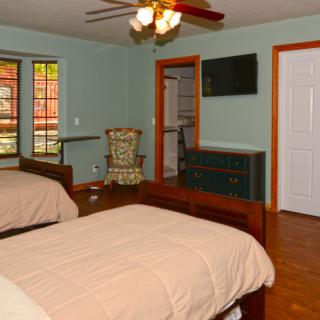 A cozy bedroom with two twin beds, a ceiling fan, and a flat-screen TV.