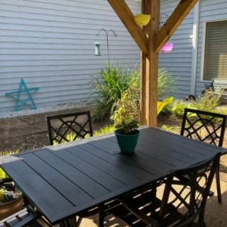 A cozy backyard patio with a wooden table and chairs under a pergola.