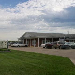 A small building with a parking lot and several cars parked, set against a cloudy sky.