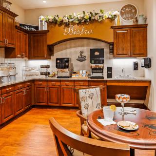 A cozy kitchen with wooden cabinets and a coffee station, featuring a small dining table set for two.