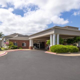 The image depicts the exterior of a building with a covered entrance against a partly cloudy sky.