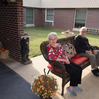 Elderly individuals sitting on a bench in a patio area outside a brick building.