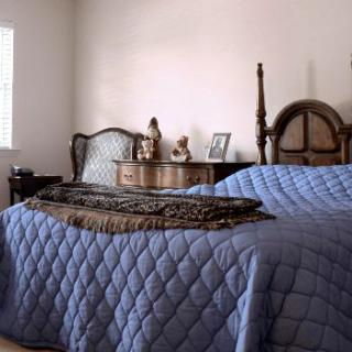 A cozy bedroom with a blue quilt-covered bed and antique furniture.