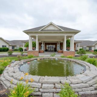 A building entrance with a landscaped pond and columns under a cloudy sky.