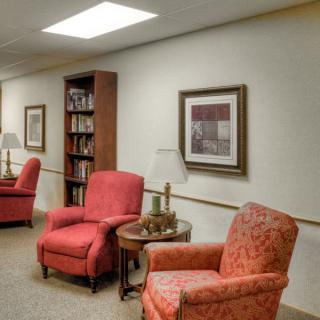 A cozy interior with red armchairs, a wooden bookshelf, and framed artwork on the wall.