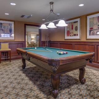 A cozy game room featuring a pool table under warm lighting with wood paneling and framed artwork on the walls.