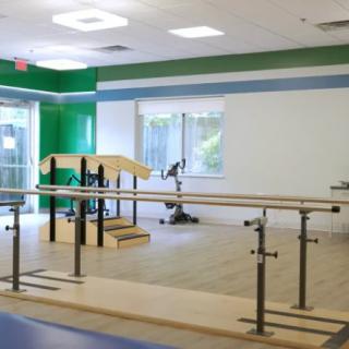 A brightly lit physical therapy room equipped with rehabilitation exercise equipment.
