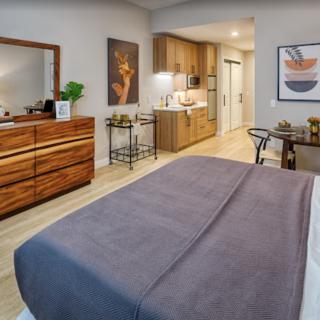 A cozy and modern bedroom with a kitchenette, featuring stylish decor and warm wooden furniture.