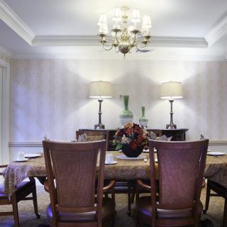 A well-decorated dining room featuring a central table, elegant chairs, and ambient lighting with a chandelier and lamps.