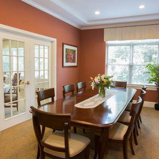 A well-lit dining room with a wooden table, chairs, and flowers on the table.