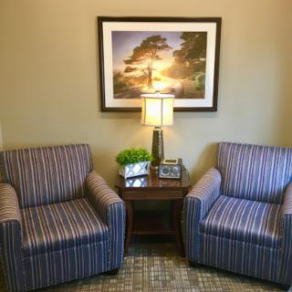 A cozy living room setup featuring two striped chairs, a table with a lamp, and a nature-themed painting on the wall.