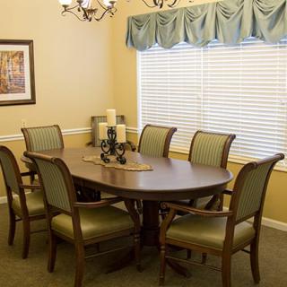 A cozy dining room with a wooden table and six upholstered chairs, decorated with candles and lit by a chandelier.
