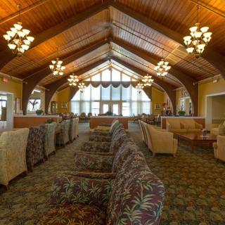 A spacious and elegantly designed lounge with a wooden ceiling, chandeliers, and upholstered seating.