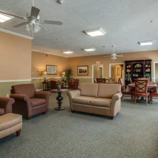 A cozy communal living area featuring sofas, armchairs, and a dining table under soft overhead lighting.