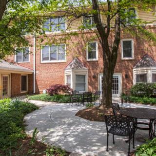 A peaceful courtyard with outdoor seating surrounded by a brick building and lush greenery.