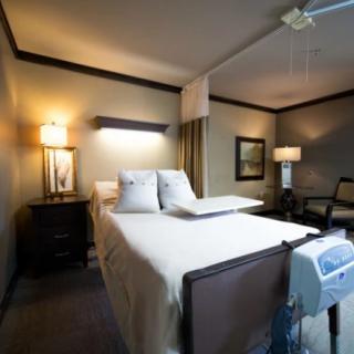 A hospital room with a bed and medical equipment, featuring warm lighting and simple furnishings.