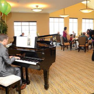 A person playing the grand piano at an indoor event with an audience seated nearby.