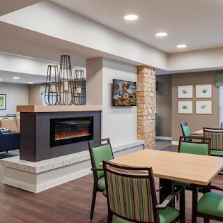 A modern interior lobby with a cozy fireplace, featuring dining tables and green chairs.