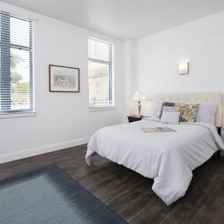A modern, minimalist bedroom with white walls and hardwood floors, featuring a neatly made bed and stylish decor.
