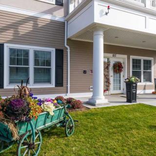 A well-maintained building entrance with a decorative wheelbarrow full of flowers and a lush green lawn.