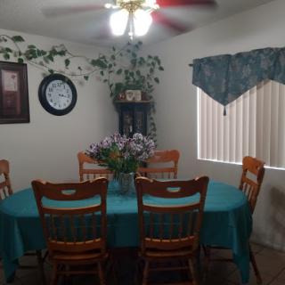 A cozy dining room featuring a round table set with a teal tablecloth, surrounded by wooden chairs and adorned with floral centerpieces.