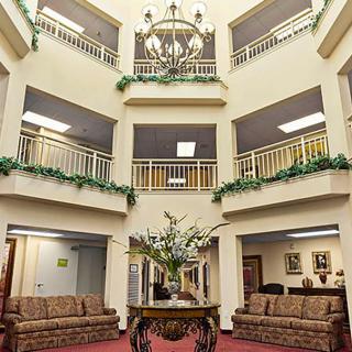 A spacious lobby area featuring a central table with floral decorations, surrounded by multiple floors and balconies adorned with greenery.
