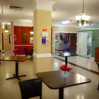 A cozy dining area with neatly arranged tables and chairs, adorned with flowers and illuminated by chandeliers.