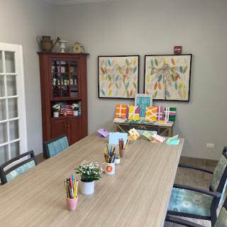 A well-organized workspace featuring a large table, decorative art, and supplies for creative activities.