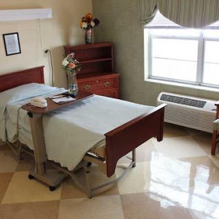 A clean and well-organized hospital patient room with a bed, storage furniture, and natural light from the window.